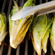 Tongs turning romaine hearts on the grill